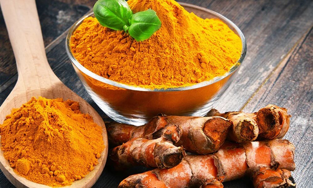 Powdered turmeric  in a bowl and on a wooden spoon